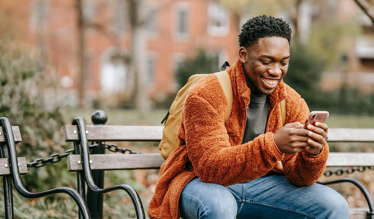 A man sitting on a bench and happily scrolling through his phone